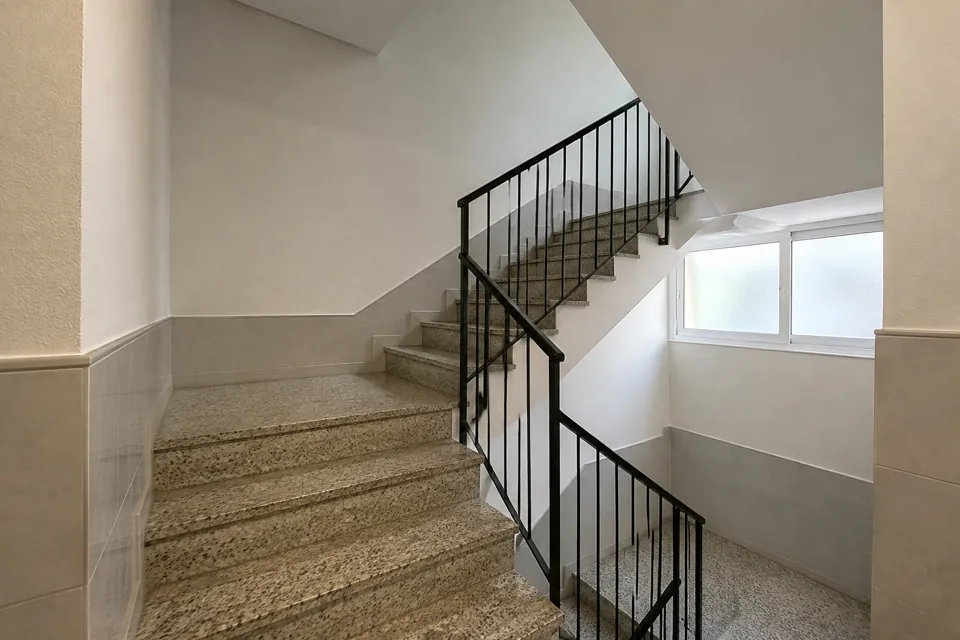 Escalera comunitaria de terrazo con barandilla metálica y luz natural